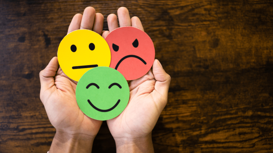 Three faces in hand - smiley face (green), neutral face (yellow) and angry face (red)