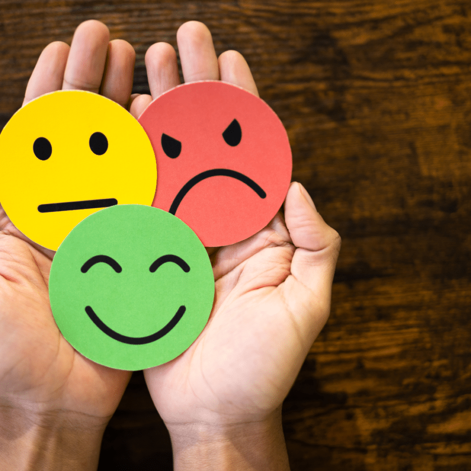 Three faces in hand - smiley face (green), neutral face (yellow) and angry face (red)